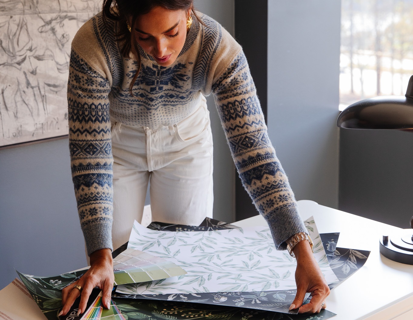 Painter holding paint can, tray and brush looks up to gable roof with creamy neutral scallop siding and gray trim.