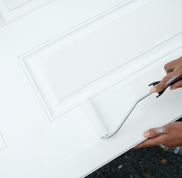 Hand holding paint roller with white paint and rolling over surface of a door.