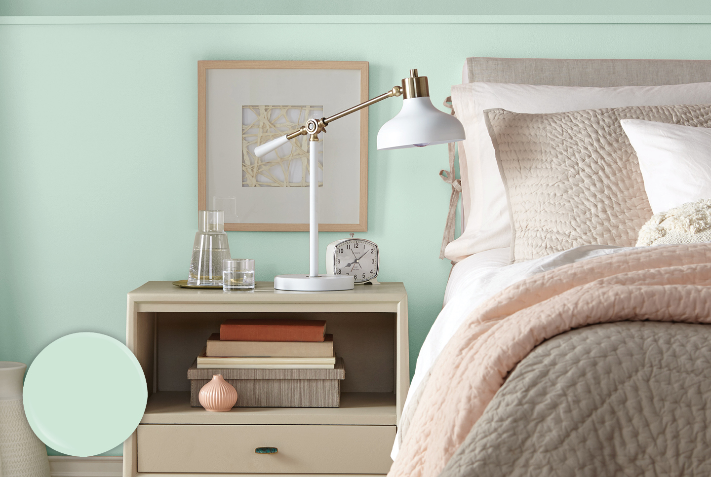 Bedside table with lamp and alarm clock against an Icy Mint wall. Bed carries neutral décor.  