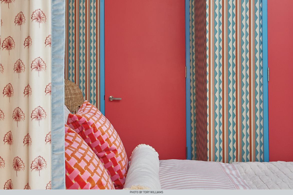 Bright, Sweet Melon door framed by striped wallpaper walls. In foreground, patterned, pink-hued pillows rest on bed.