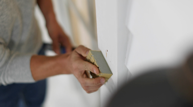 Person sanding wall with sponge.